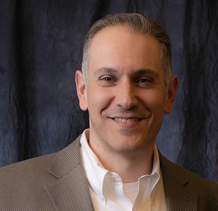 Rob Giganti, Engineering Manager and AWS Solutions Architect, in professional business attire, smiling at the camera in a modern office environment